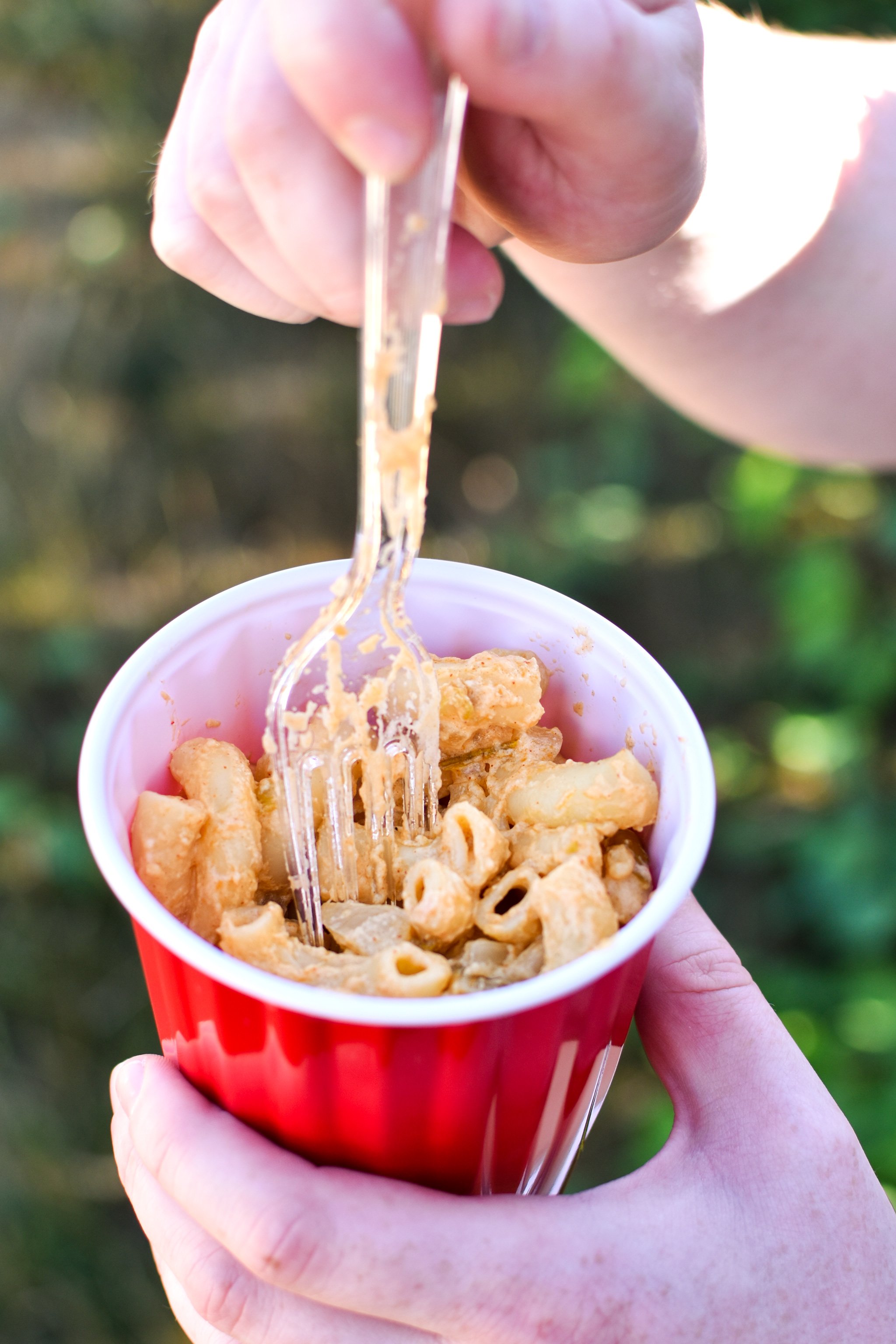 A cup of smoky white cheddar camping mac and cheese in a solo red cup with a plastic fork.