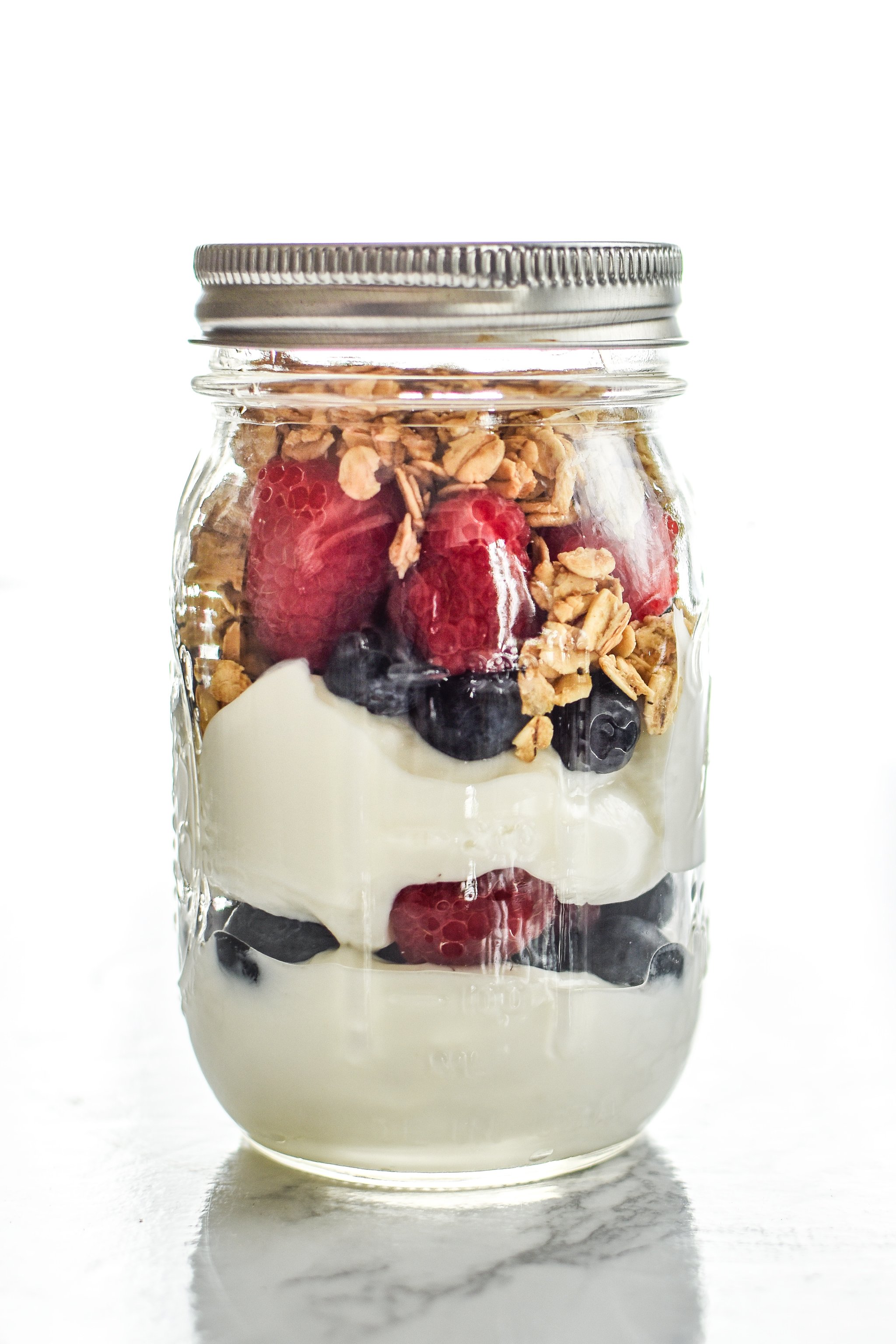 A greek yogurt parfait with granola and fresh berries in a mason jar.