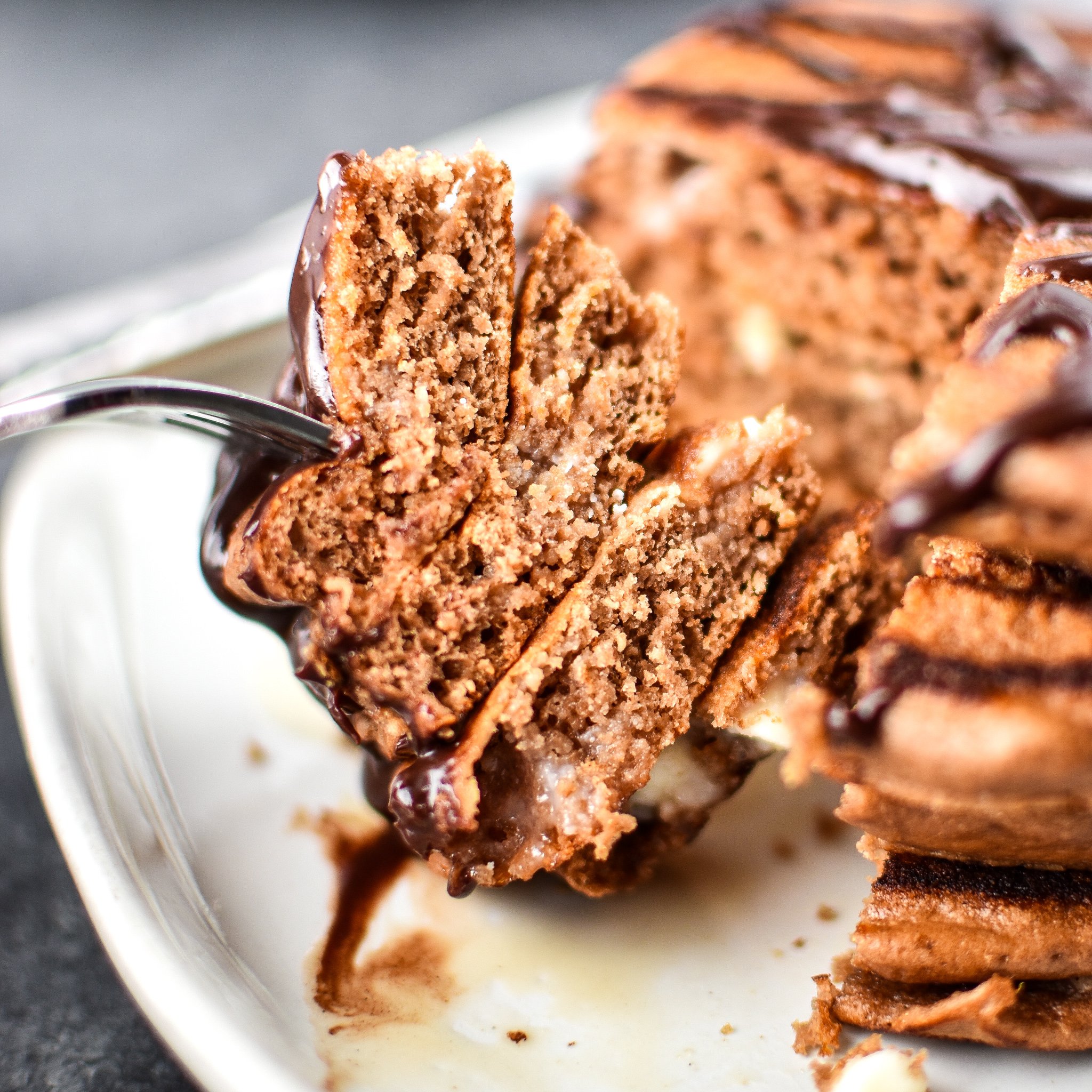 A fork piercing a big stack of Double Chocolate Peppermint Protein Pancakes drizzled with chocolate syrup.