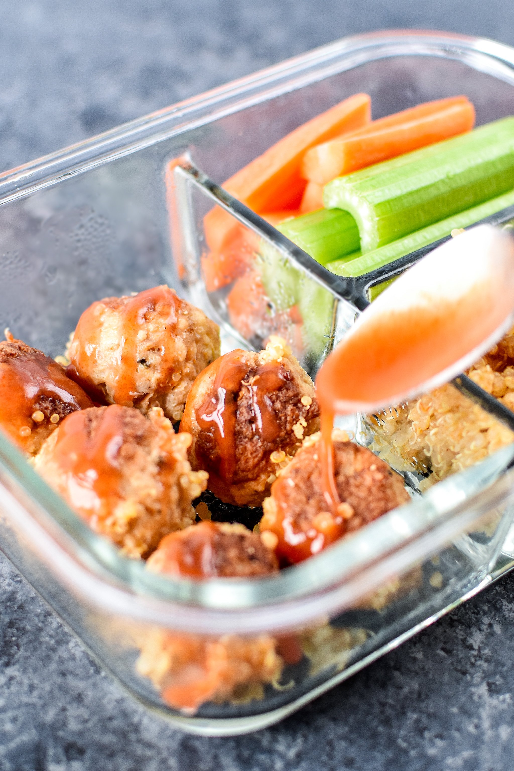 Drizzling buffalo sauce on the meal prepped meatballs.