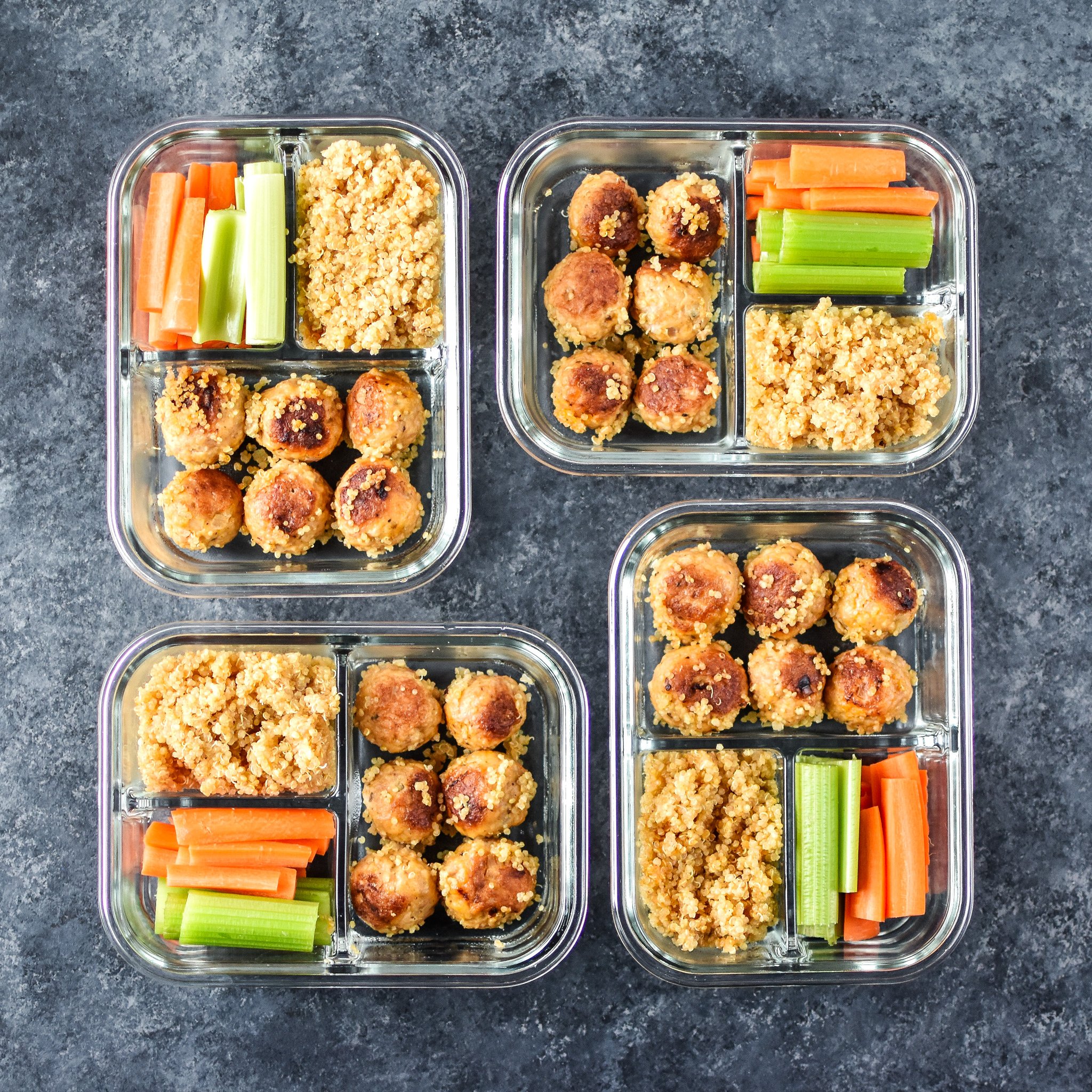 Four meal prep meatballs, quinoa and raw veggies lunches in glass containers. 
