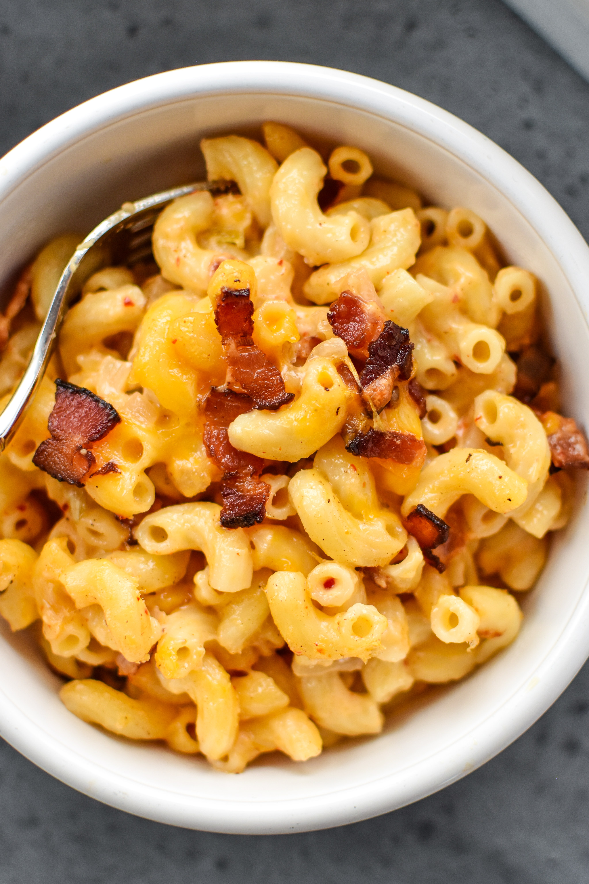 A bowl of kimchi bacon greek yogurt mac and cheese with bacon bits on top.
