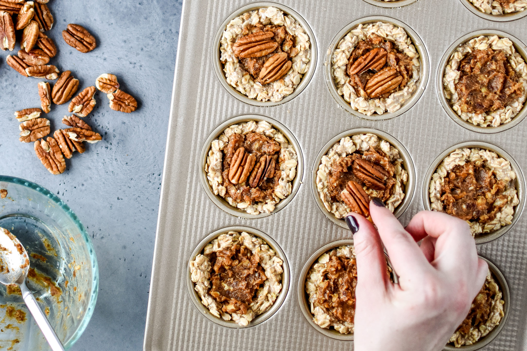 Topping the Pecan Pie Stuffed Oatmeal Breakfast Cups with pecans.