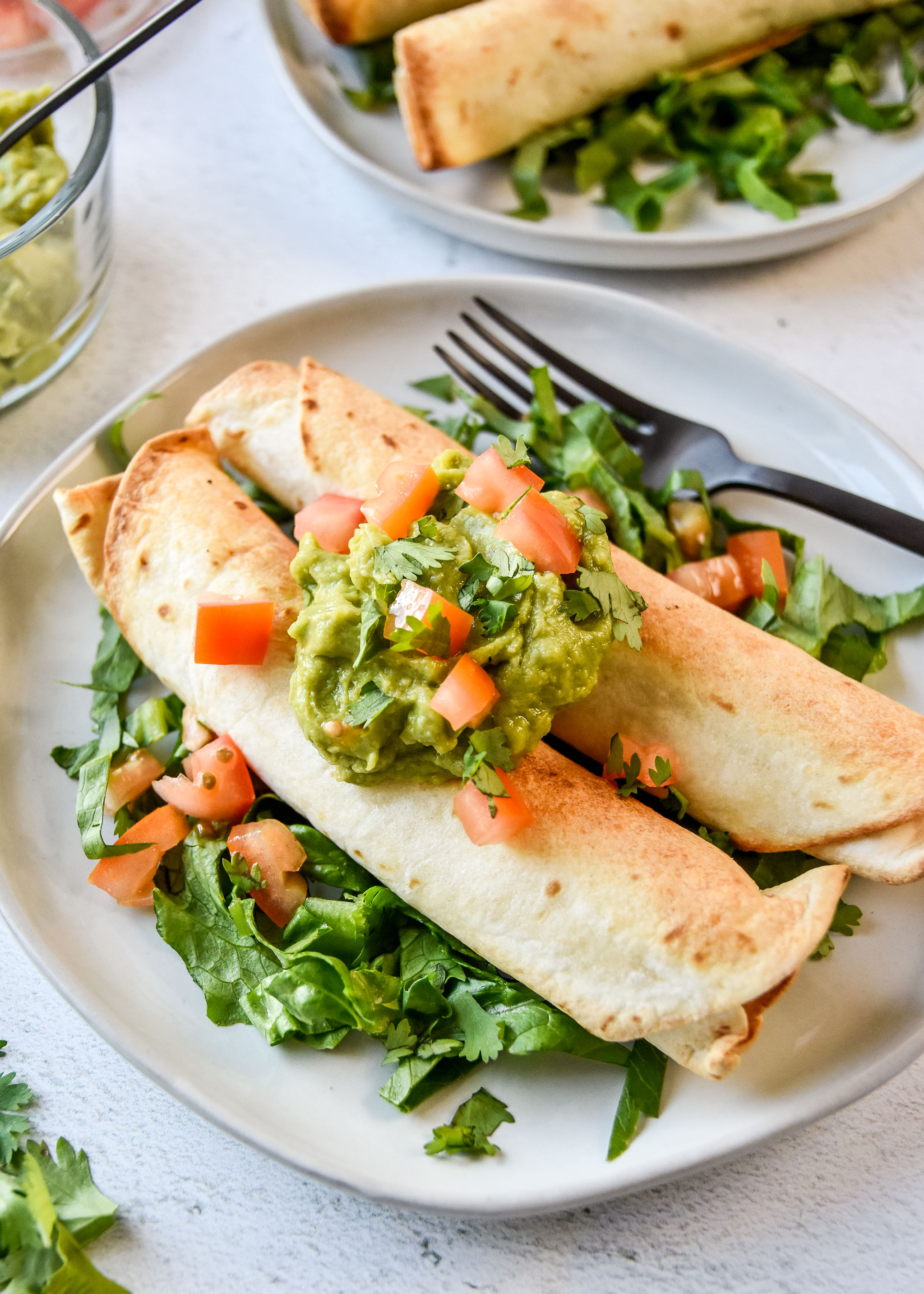 air fryer chicken taquitos topped with guacamole, tomatoes and cilantro