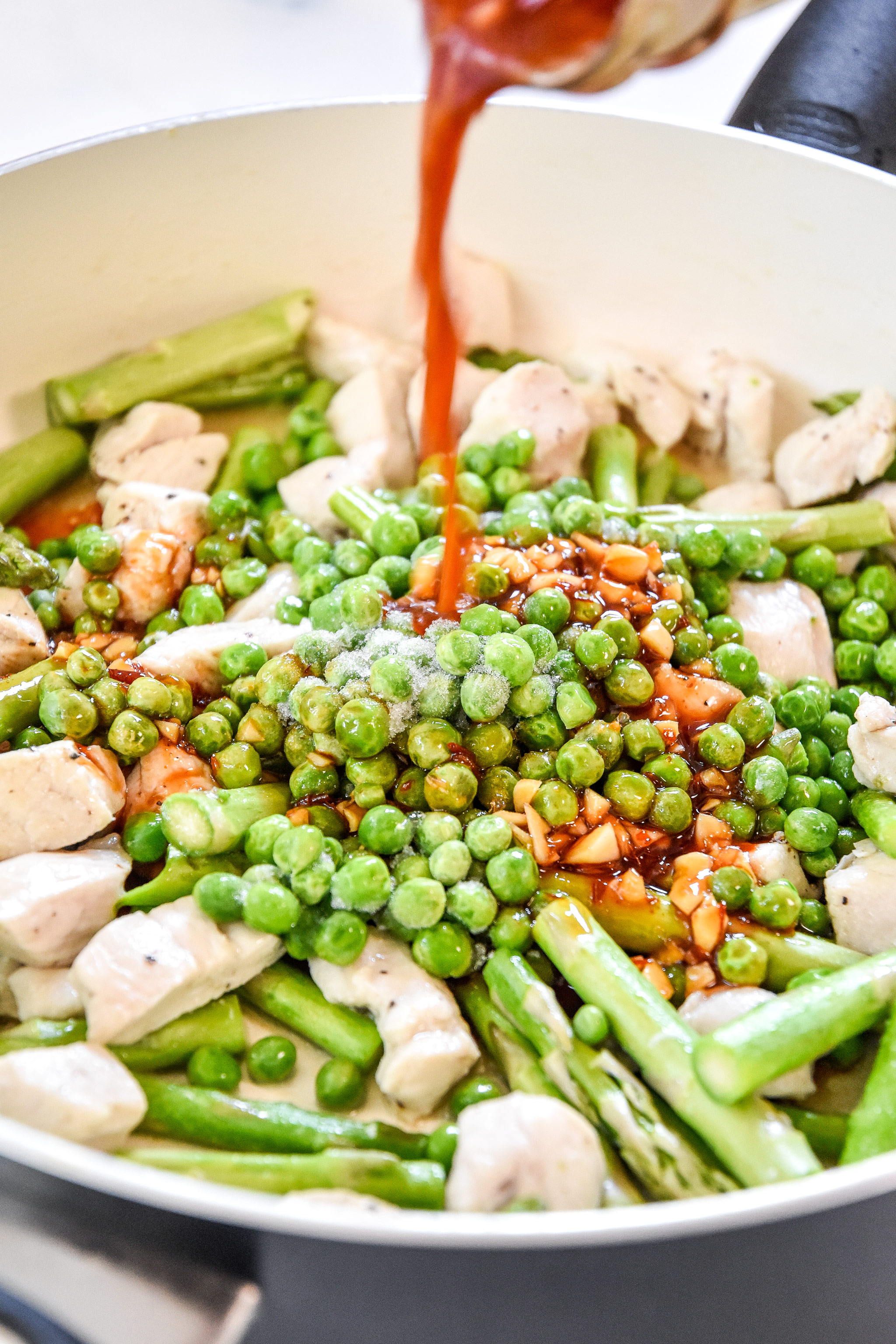 pouring sauce into the pan with the chicken asparagus and peas