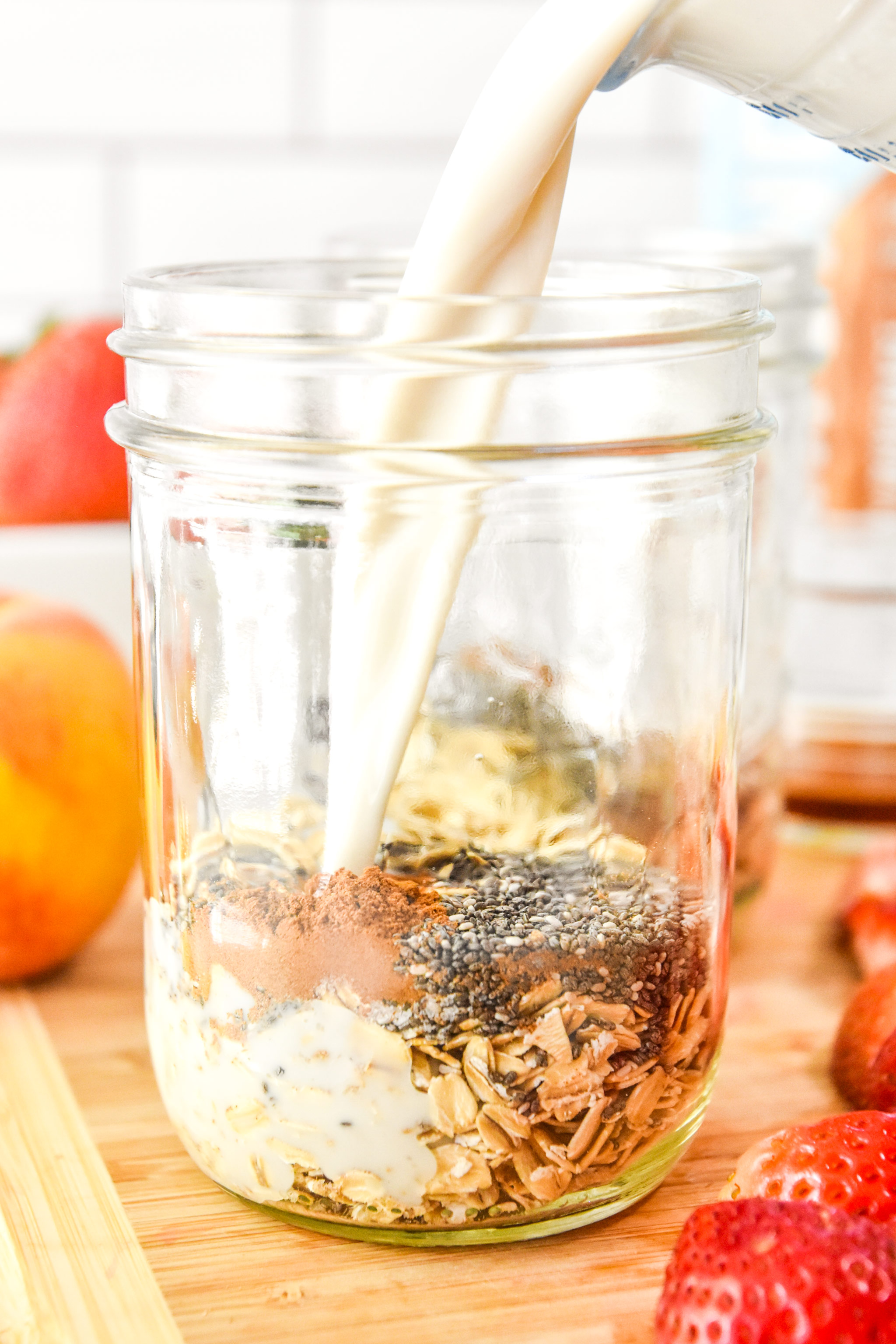 pouring milk into the mason jars for each serving of strawberry peach overnight oats.