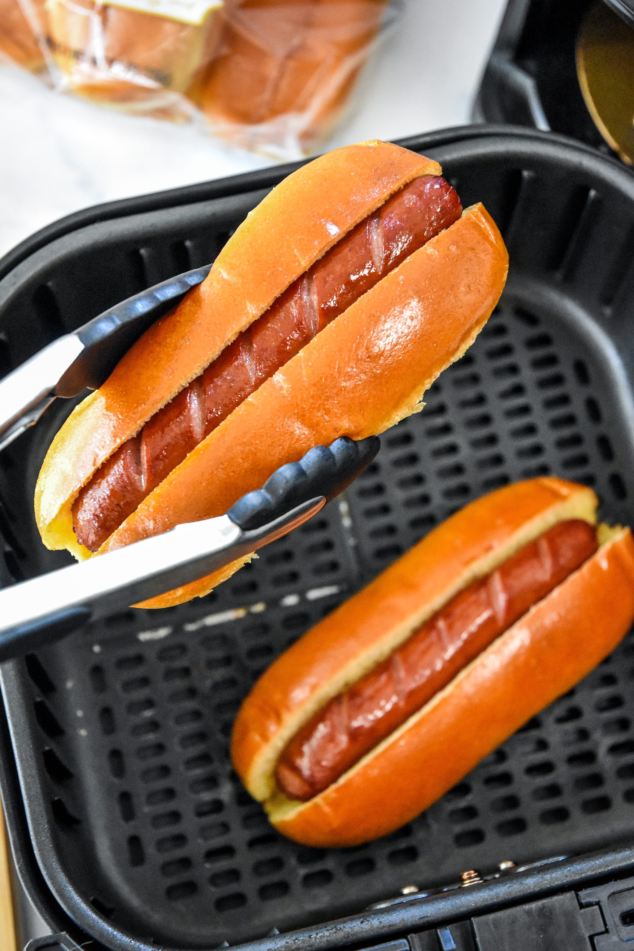 buns and hot dogs going into the air fryer basket.