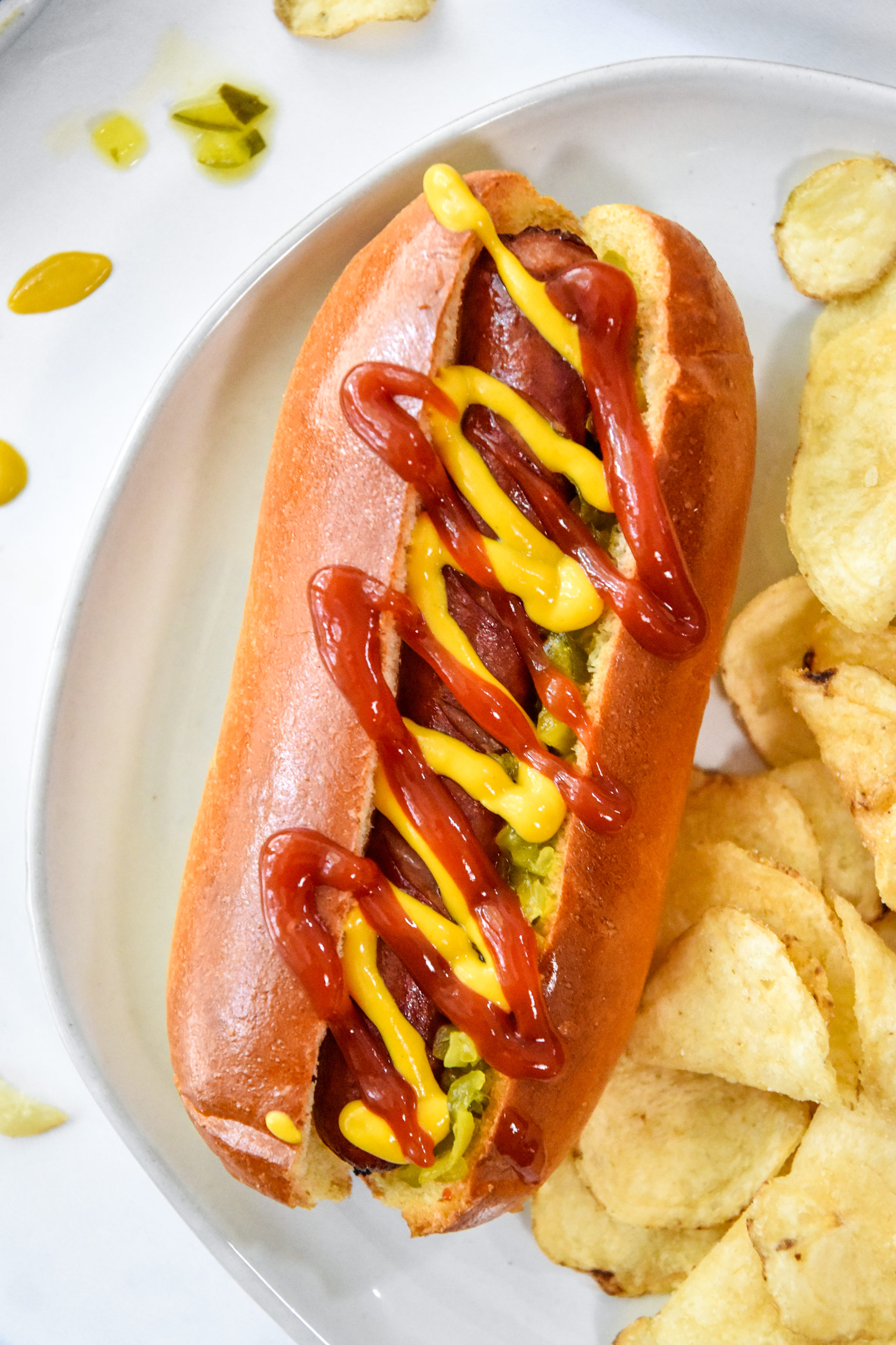 air fryer hot dog in a bun with mustard and ketchup, chips on the side.