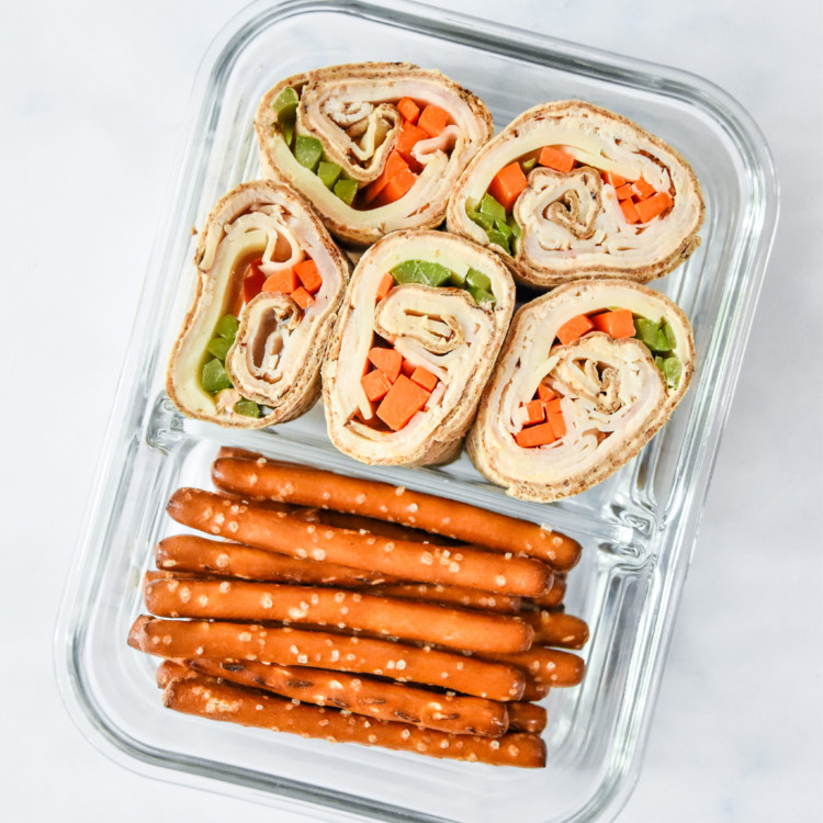 glass container with buffalo chicken pinwheels meal prep and pretzels.