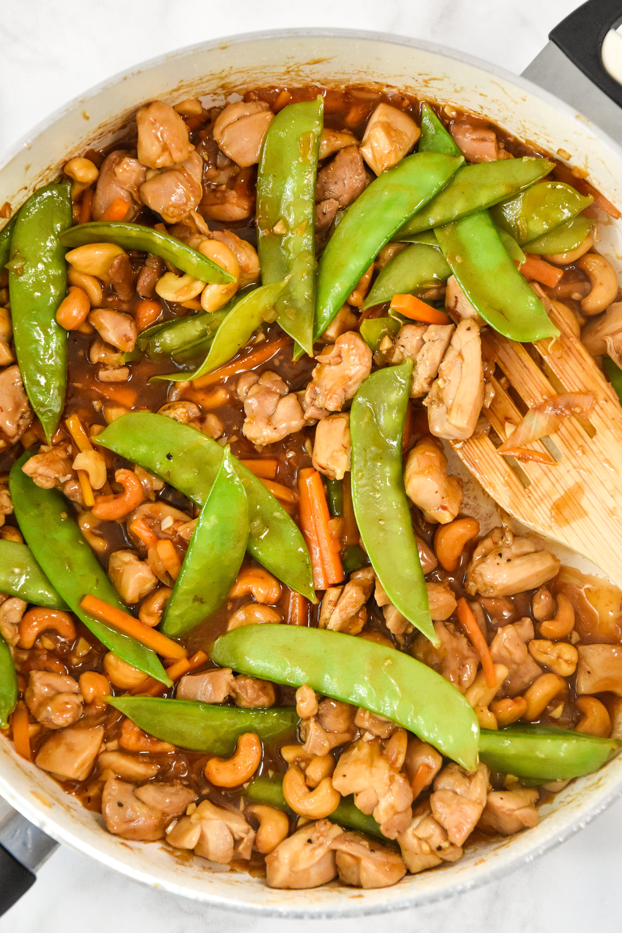 cooked easy cashew chicken on the stovetop with peas and carrots.