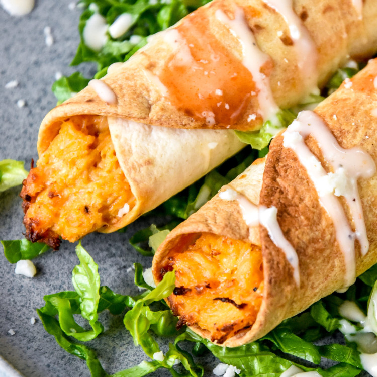 plated air fryer buffalo chicken flautas or taquitos with shredded lettuce and buffalo sauce.