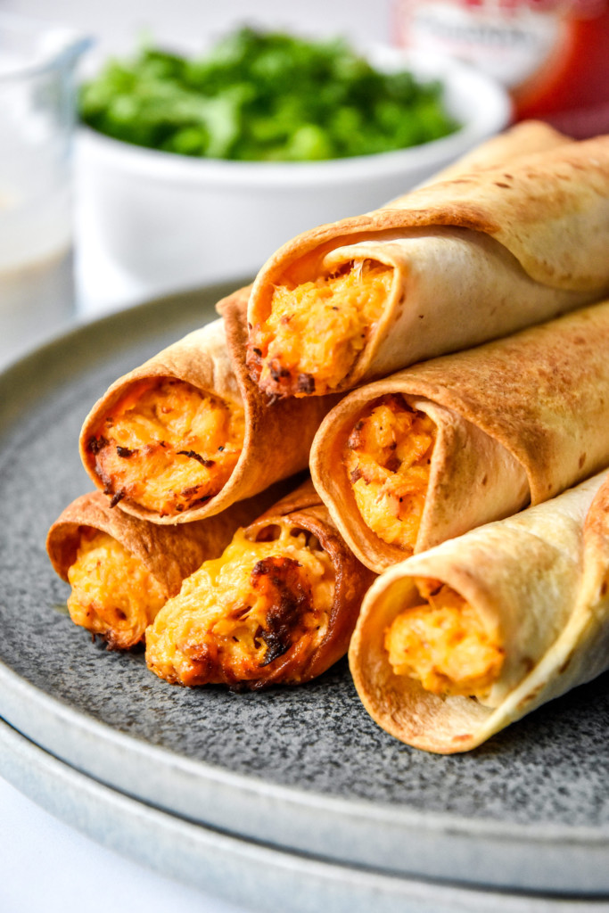 air fryer buffalo chicken flautas cooked and stacked on a plate.