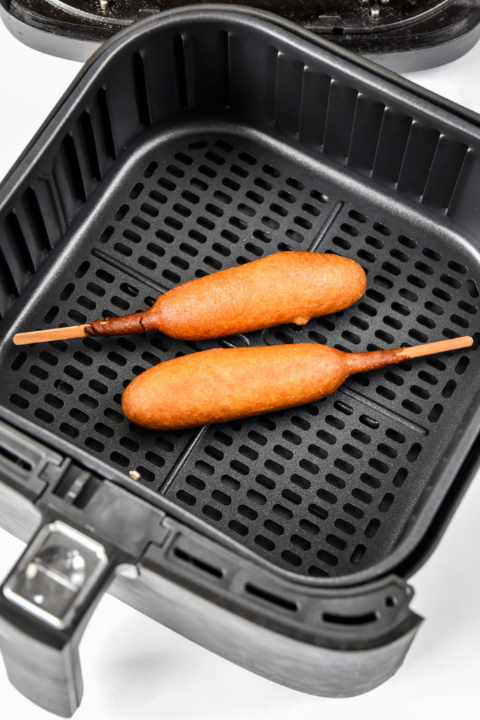 two cooked corn dogs in an air fryer.