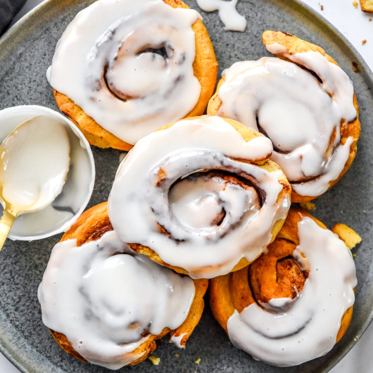 5 air fryer canned cinnamon rolls on a plate with frosting.
