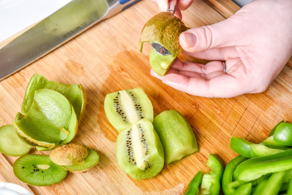 peeling a kiwi fruit with a metal spoon for the green food lunch box meal prep.