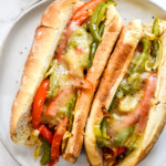 two air fryer sausage dogs with peppers and onions and melt cheese on a plate.