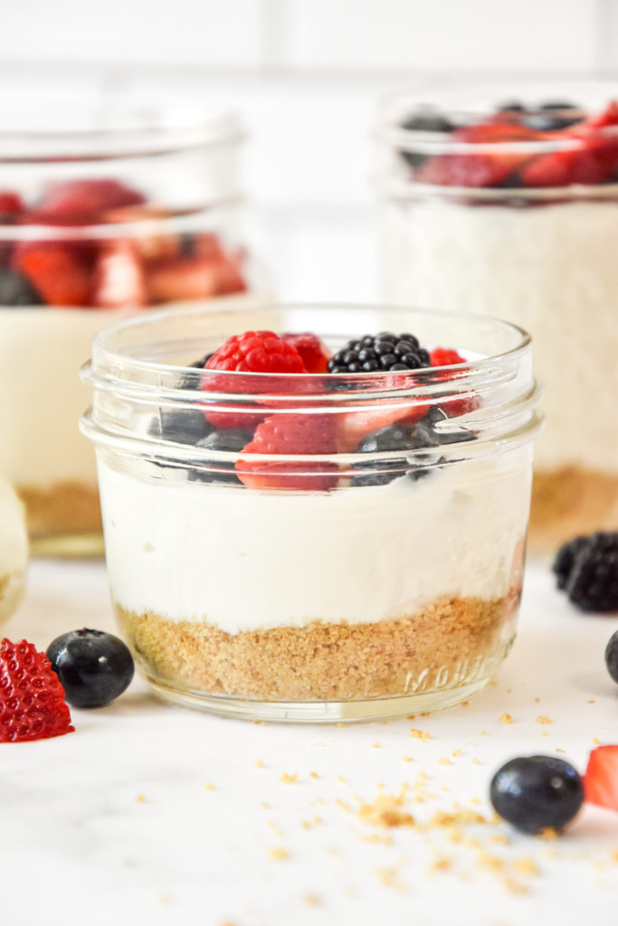no-bake cheesecake greek yogurt cups in a mason jar with fresh berries on top.