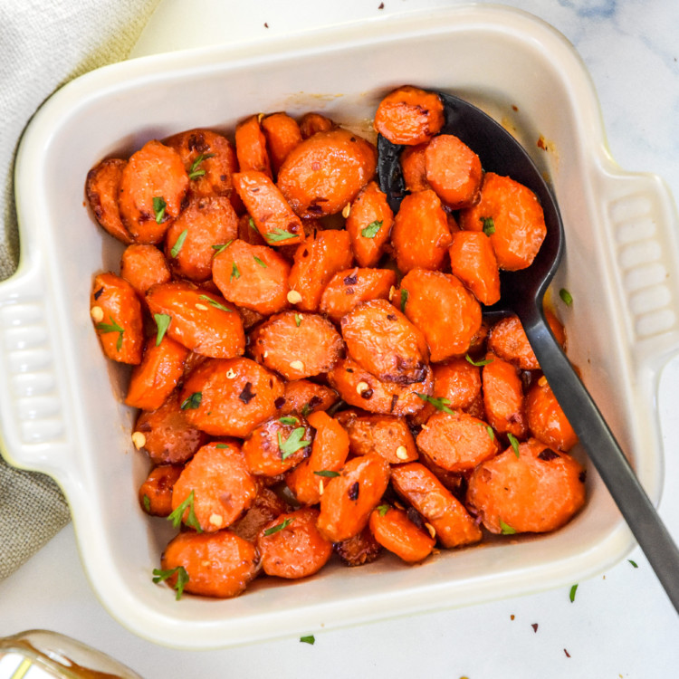 air fryer hot honey glazed carrots in a bowl with a black serving spoon.