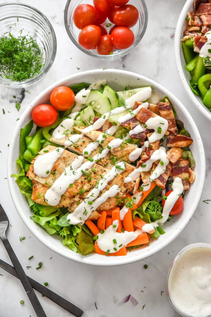 prepared go-to chicken bacon ranch salad in a white bowl with ranch dressing and herbs on top.