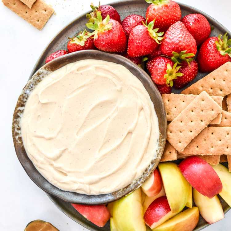 peanut butter greek yogurt fruit dip in a bowl with cut apples and strawberries.