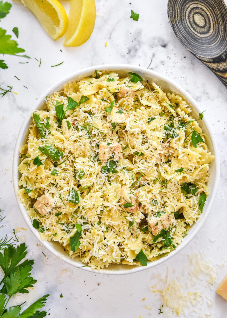 herby lemon chicken pasta salad in a white bowl with fresh herbs and parmesan on top.