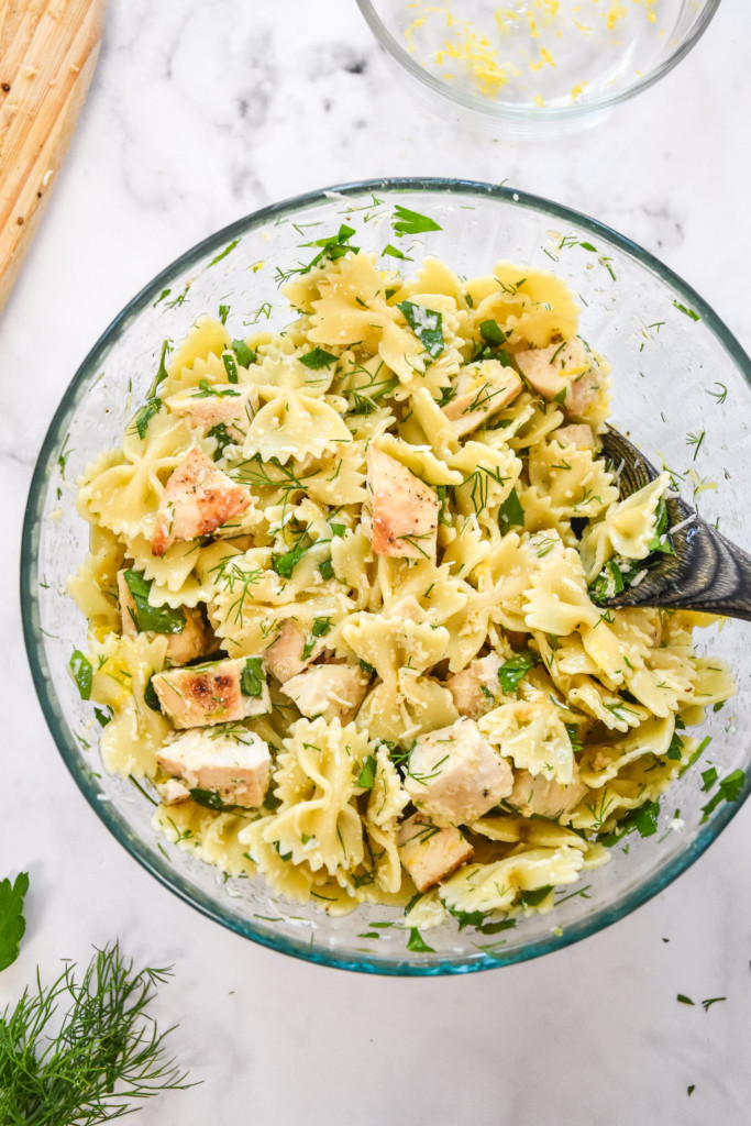 mixed up herby lemon chicken pasta salad in a glass bowl. 