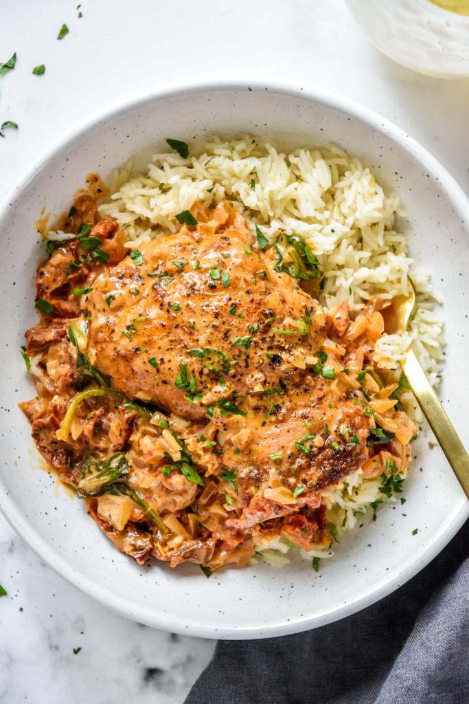 dished up creamy tuscan chicken meal prep with rice in a white bowl with gold fork.