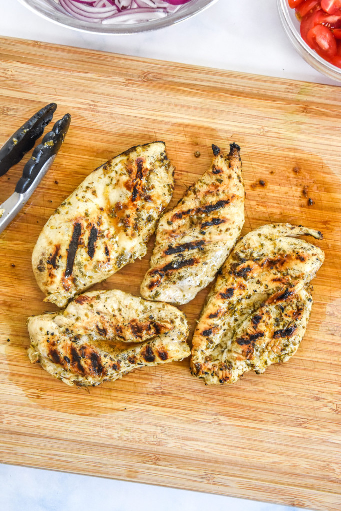 cooked charred greek chicken resting on a cutting board.