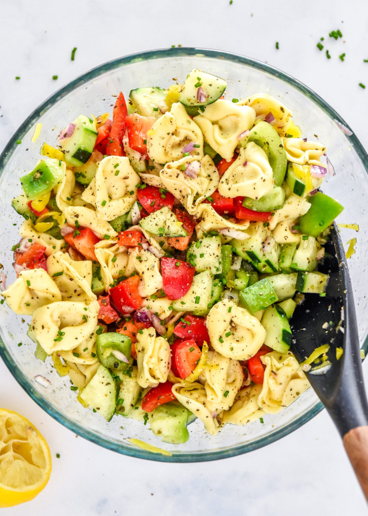 zesty italian tortellini pasta salad in a glass bowl with serving spoon.