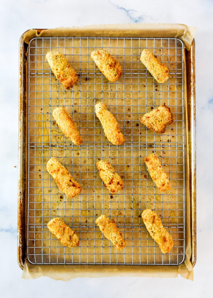 baked homemade fish sticks fresh out of the oven on a rack and baking tray.