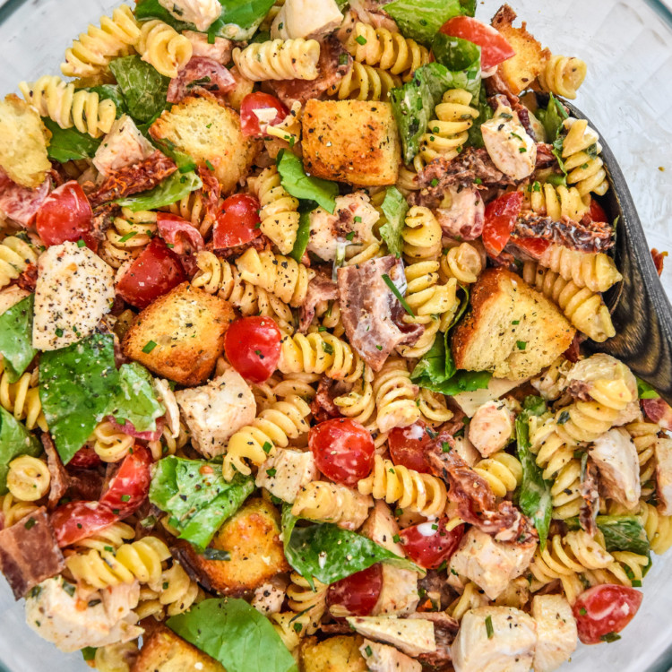 make-ahead chicken club pasta salad in a large glass serving bowl with spoon.