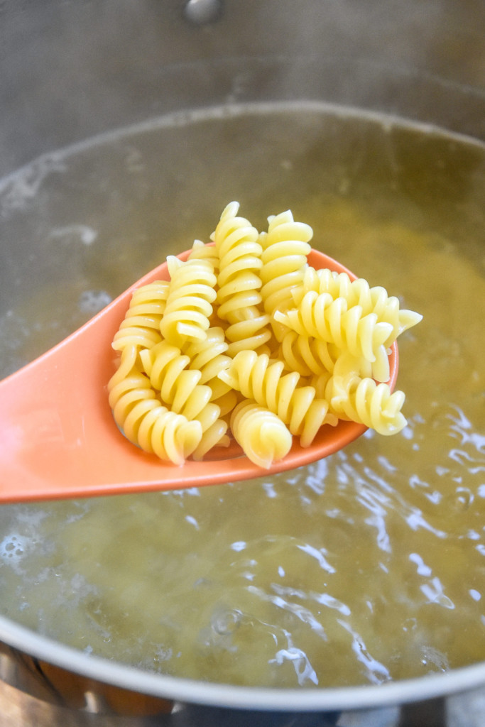 cooked pasta in a slotted spoon over a pot of boiling water.