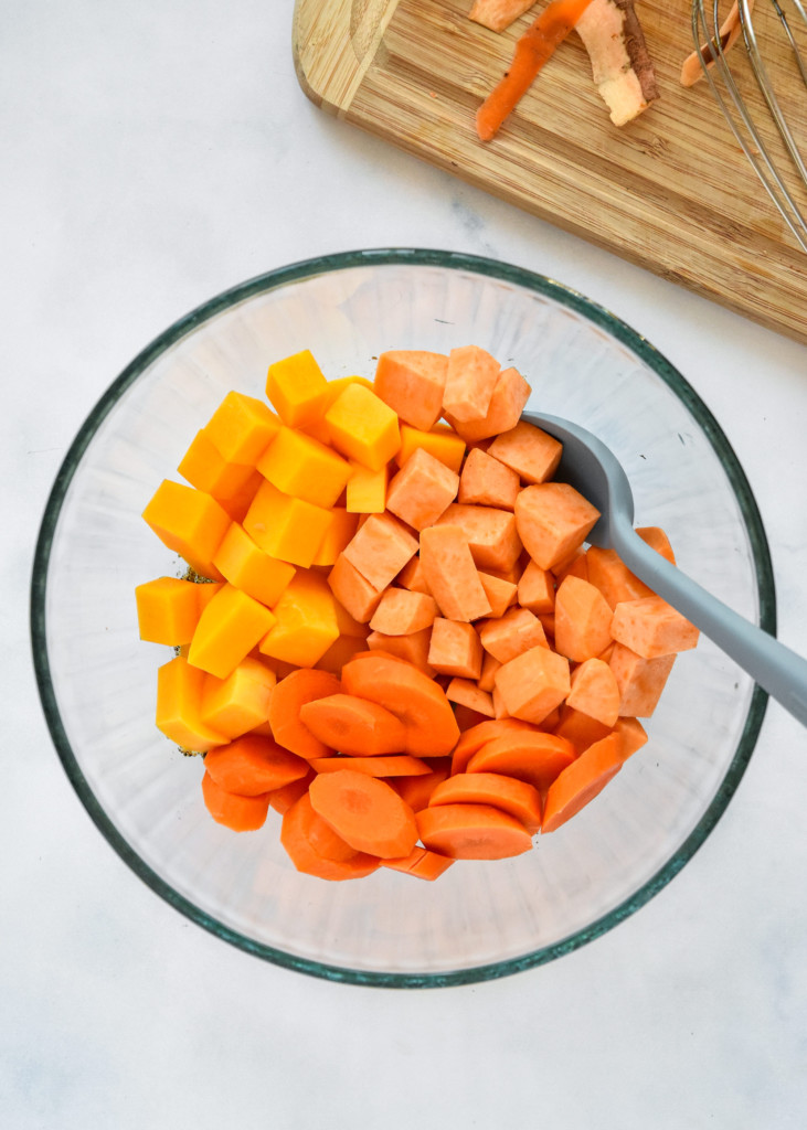 cut squash, sweet potatoes, and carrots in a glass bowl before roasting.