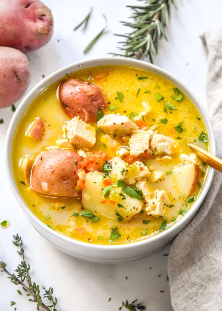simple red potato chicken soup in a round bowl with a gold spoon.