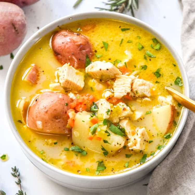 simple red potato chicken soup in a round bowl with a gold spoon.