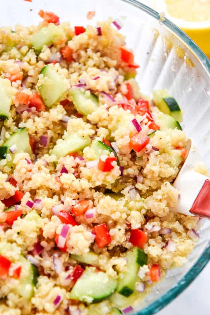 make-ahead quinoa party salad in glass bowl with mixing spatula.
