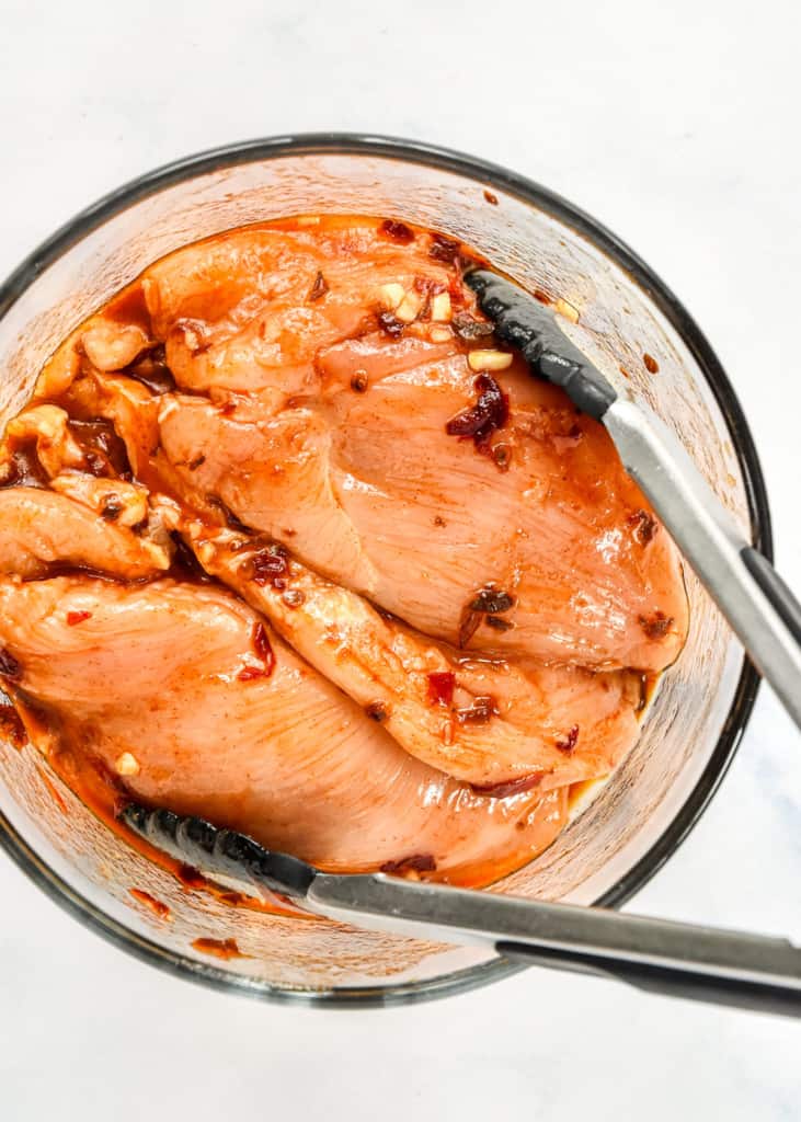 marinating chicken in a large glass bowl with tongs.