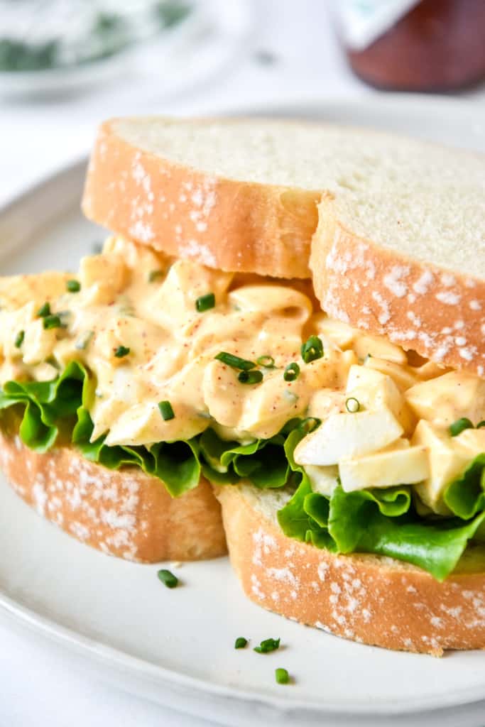 Easy Deviled Egg Salad on white bread with lettuce and chives.