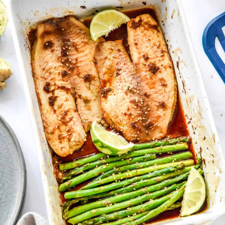 fresh from the oven ginger soy tilapia with broiled asparagus in a shallow white baking dish.