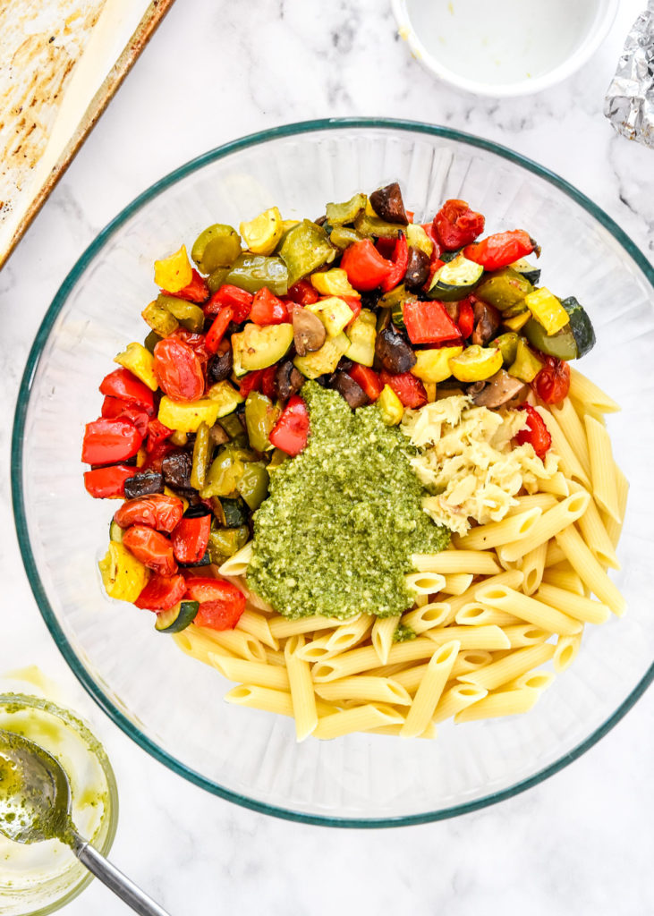 roasted vegetables, pasta and pesto in a large bowl before mixing.