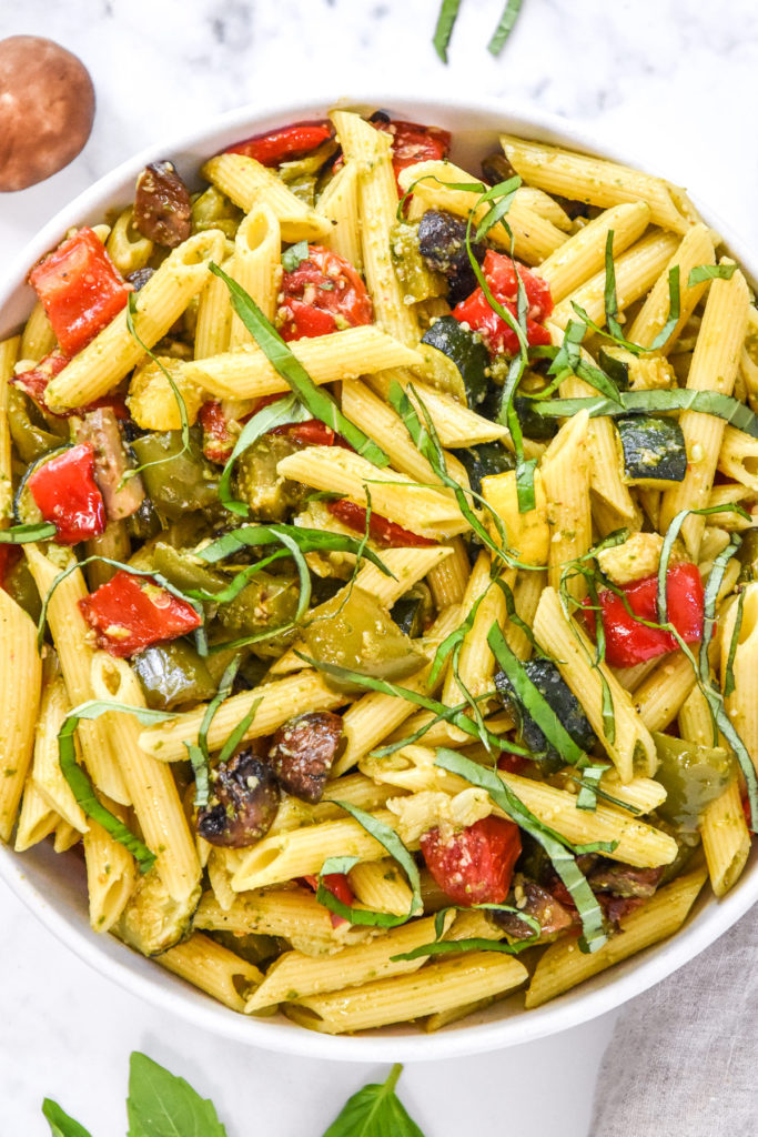 roasted veggie pesto pasta salad in a bowl with basil on top.