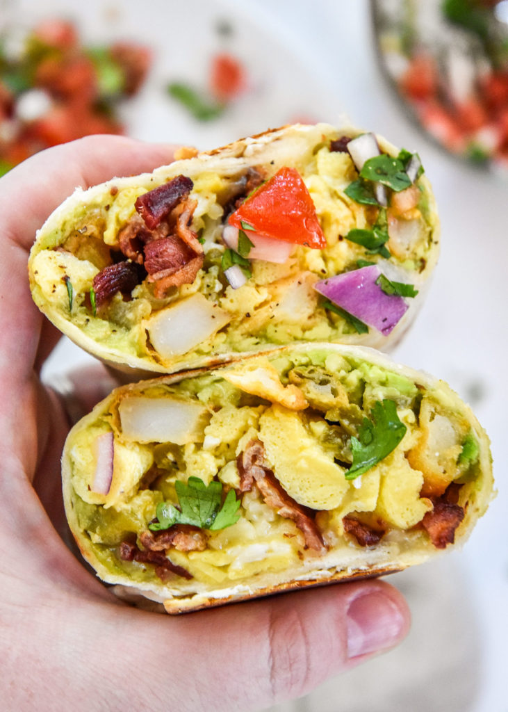 holding a meal prep california style breakfaas burrito in hand.