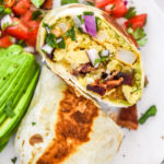 california style breakfast burrito browned and cut in half on a white plate.