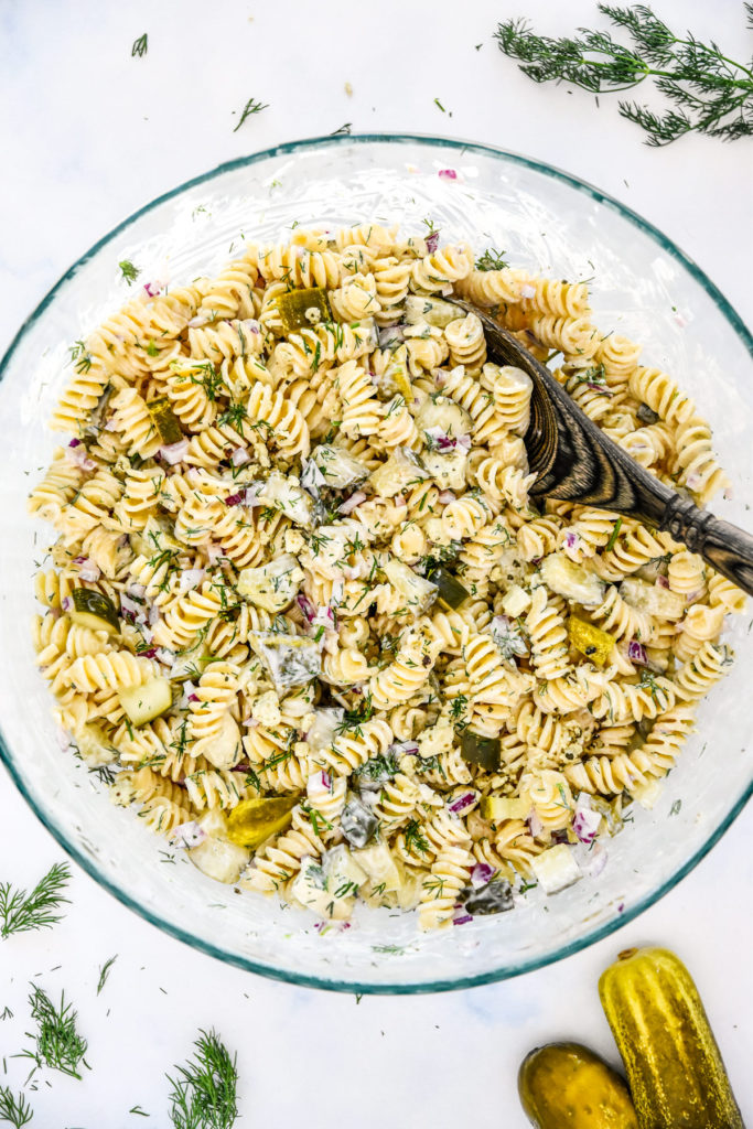 creamy dill pickle pasta salad in a large glass serving bowl with wooden spoon.