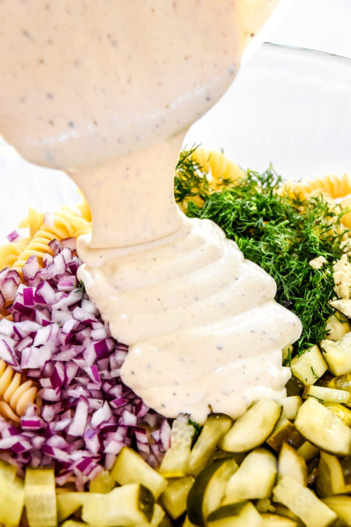 pouring dressing into the dill pickle pasta salad bowl.