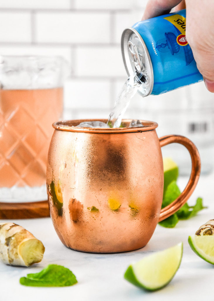 pouring soda water into a copper mug for a moscow mule.