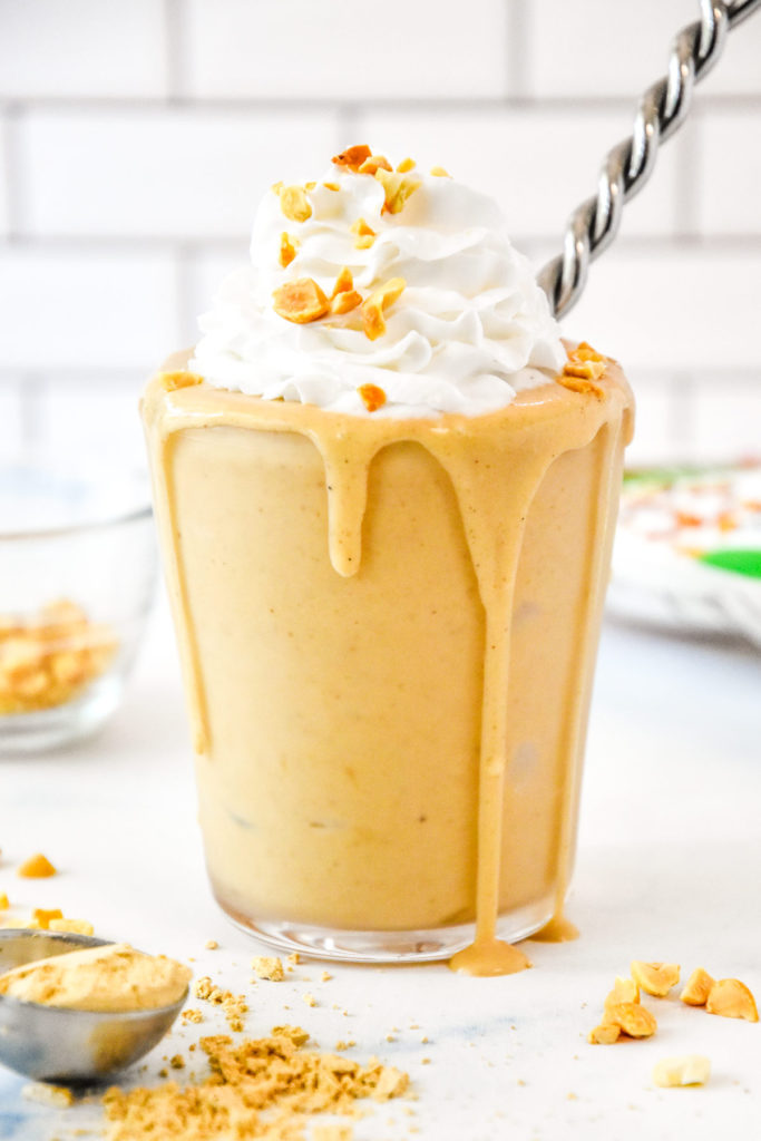 A Peanut Butter Powder Milkshake in a clear cup with whipped cream and chopped peanuts on top.