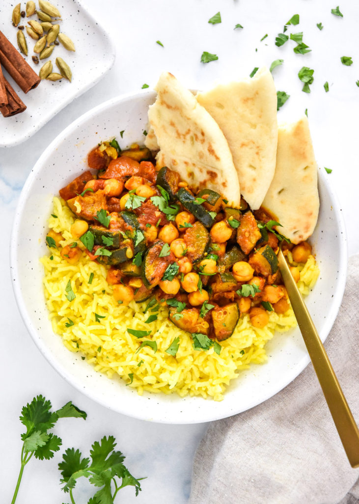 zucchini chickpea curry meal prep in a bowl with turmeric rice and naan bread.