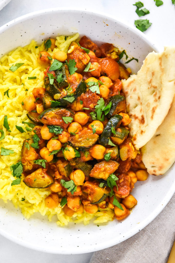 zucchini chickpea curry meal prep in a bowl with turmeric rice and naan bread.