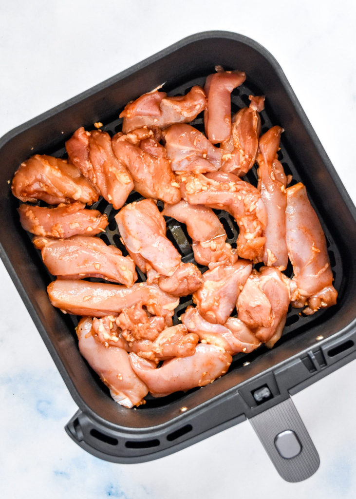 raw marinated chicken in an air fryer basket before cooking.